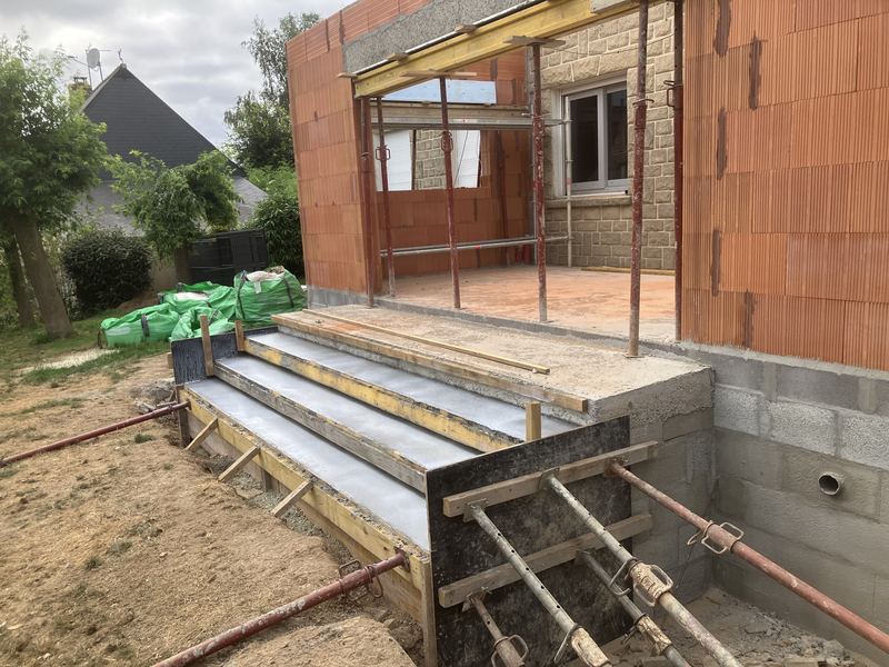 Escalier en béton coffré devant une extension en brique, en chantier