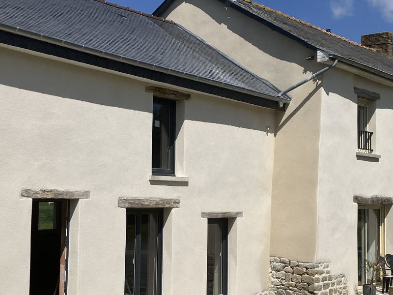 Façade de longère enduite à la chaux, linteaux en bois et soubassement en pierre