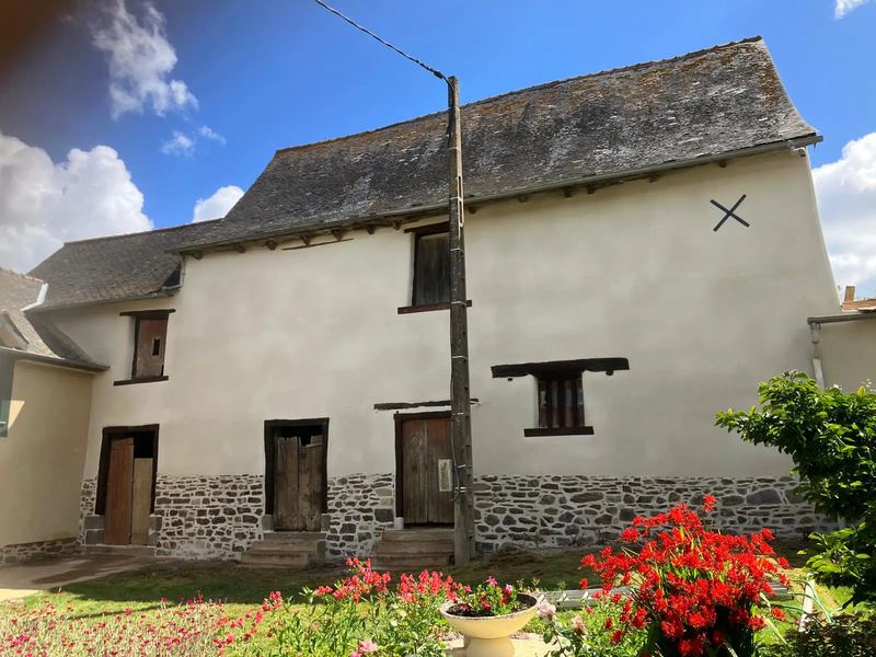 Façade de longère enduite à la chaux, soubassement en pierre et fleurs au pied du mur
